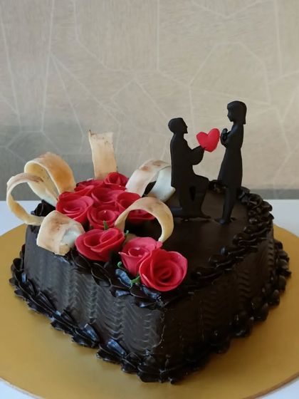 A classic heart-shaped chocolate cake for a proposal or anniversary. It's decorated with red sugar roses and a silhouette of a couple, symbolizing a romantic moment.