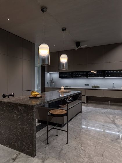 Set in an Ahmedabad farmhouse, this kitchen has a soft monolithic feel. Floor-to-ceiling cabinetry in Calgary Laminate and a sculpted dark stone island create a sense of weight and clarity.