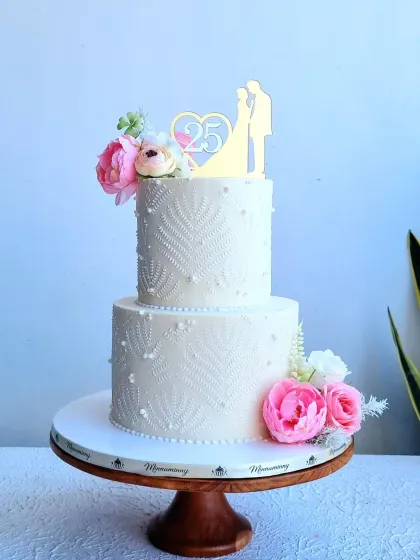 A full view of the two-tiered white anniversary cake, showing the delicate lace stenciling.
