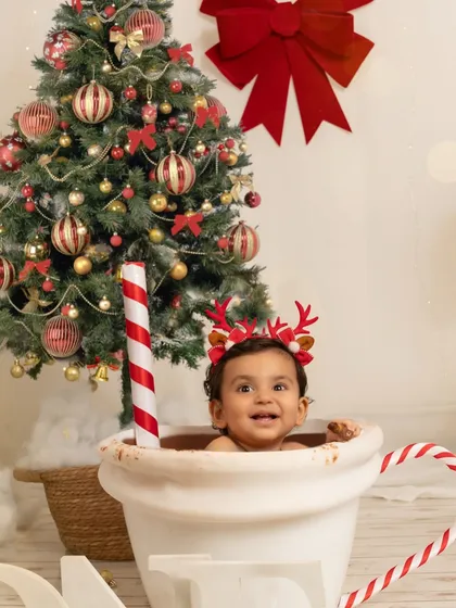 A close-up of the baby's happy face as he sits in the mug, wearing reindeer antlers, perfectly capturing the joy of his first Christmas.