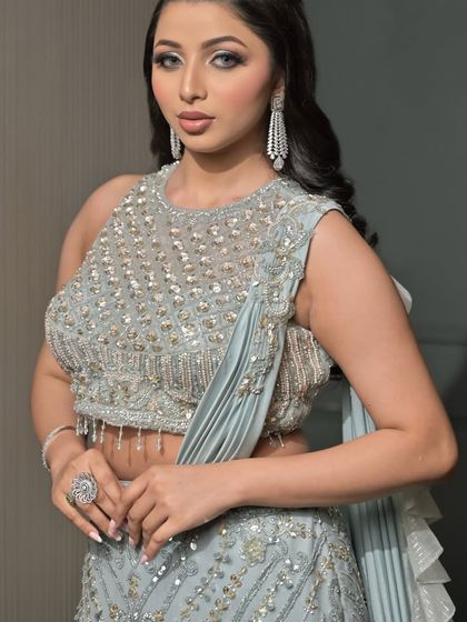 A powerful and confident pose in a modern, heavily embellished outfit. The makeup is kept sharp and glamorous with a defined smokey eye and contoured features.