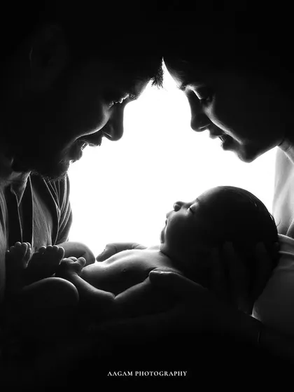 A silhouette of a new family, their faces illuminated as they gaze lovingly at their baby. This is a powerful, emotional image of a family born in a single moment.