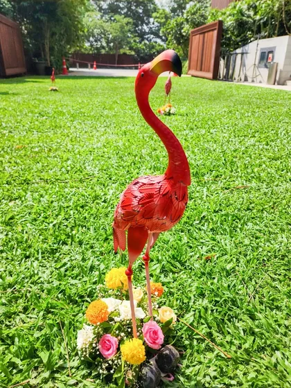 A playful and quirky decor element for an outdoor Mehendi party. This bright pink flamingo statue, surrounded by a ring of colorful flowers, adds a fun and unexpected touch to the lawn.