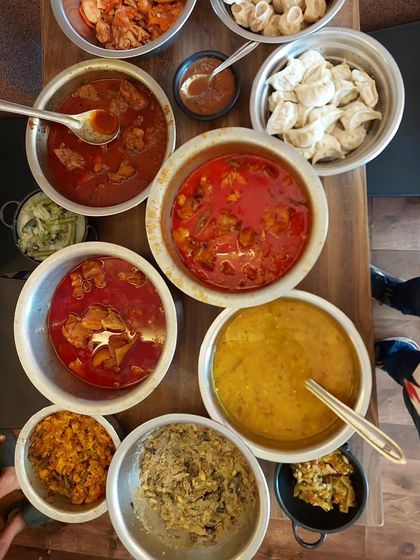A top-down view of a family-style meal at our restaurant. You can see bowls of different pork and chicken curries, dal, and fresh momos, showing the variety we offer.