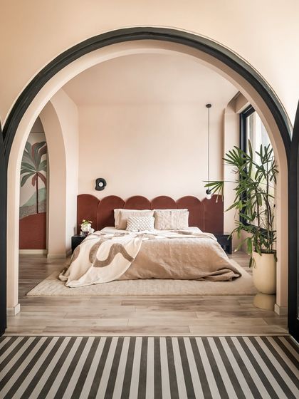 This bedroom in the "House of Mousse" is a peaceful retreat. The bed is framed by black arches, creating a cozy, intimate feel while offering a view of the striped terrace and greenery outside.