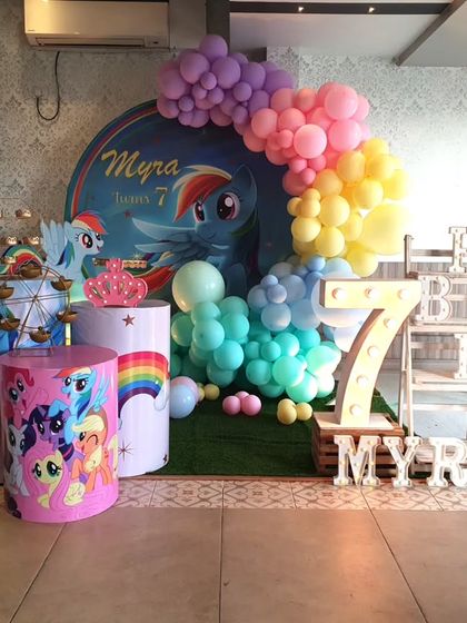 A whimsical My Little Pony-themed seventh birthday. The decor features a Rainbow Dash backdrop, a rainbow balloon arch, and a large light-up number '7'.