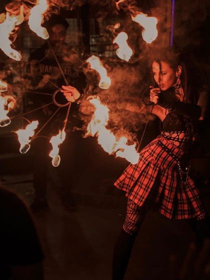 A performer channels a punk rock aesthetic with fire fans. The combination of the plaid skirt and the raw fire creates a rebellious and energetic vibe, perfect for alternative events and music festivals.
