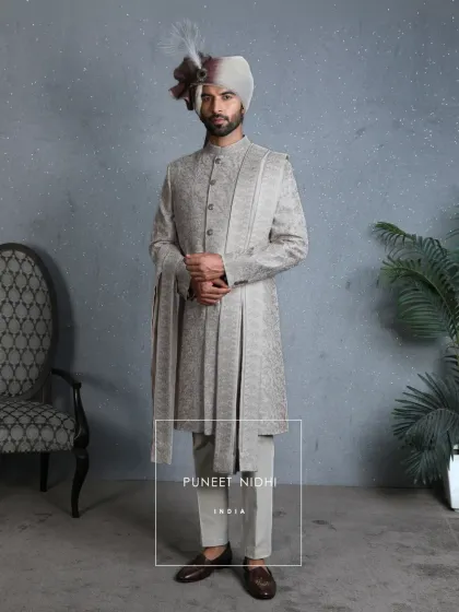 In the subtle glow of coffee beige lies a canvas of regal artistry. Jacquard-woven vines and intricate aariwork merge seamlessly into a bandhgala silhouette, creating a timeless emblem of majesty.