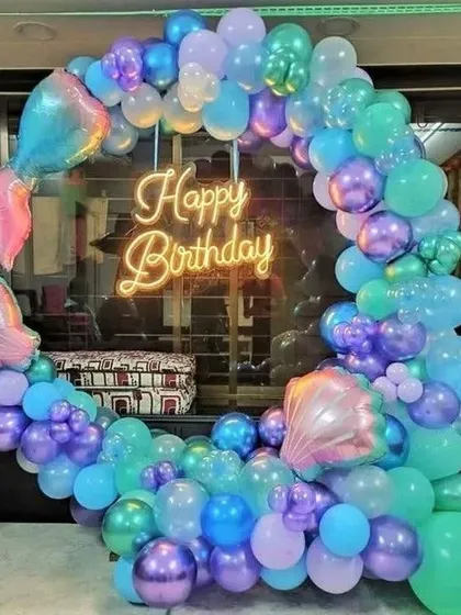 A mermaid-themed birthday party with a circular balloon arch in purple and teal, complete with a mermaid tail foil.