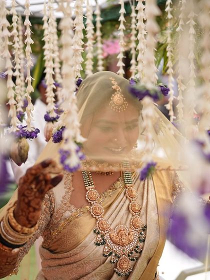 An artistic shot of a bride looking through her veil. Her golden saree and heavily embroidered blouse are visible, creating a soft and romantic image.