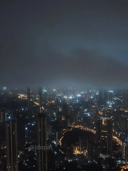 A drone's perspective of Mumbai at night, with the city lights partially obscured by low-hanging monsoon clouds.