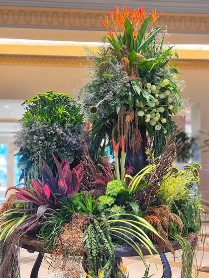 This arrangement uses a mix of dried and fresh foliage in various colors, from deep greens and burgundies to earthy browns, creating a rich and complex tapestry.