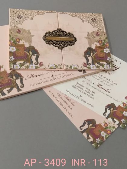 A simple and elegant invitation in blush pink, featuring decorated elephants and a traditional border. This affordable card comes with two inserts, perfect for the main ceremony and reception.