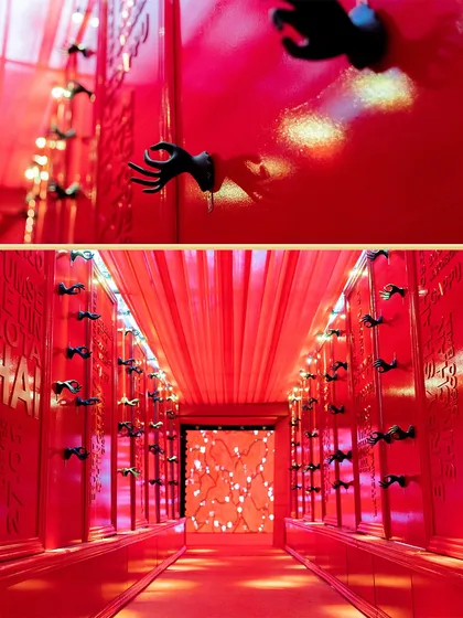 A bold and enchanting entrance for a 'Red Room' themed Sangeet. The corridor is bathed in red light, with unique hand sculptures lining the walls, creating a dramatic and immersive experience from the very first step.