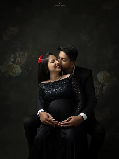 An intimate moment between an expecting couple in our studio. The dark, moody lighting and the woman's elegant black sequined gown create a romantic and glamorous atmosphere for a maternity couple shoot.