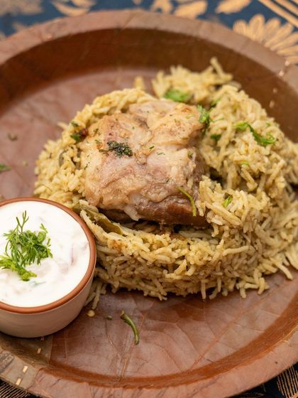 A beautifully plated Bannur Mutton Palav, served on a traditional leaf plate with a side of cooling onion raitha.