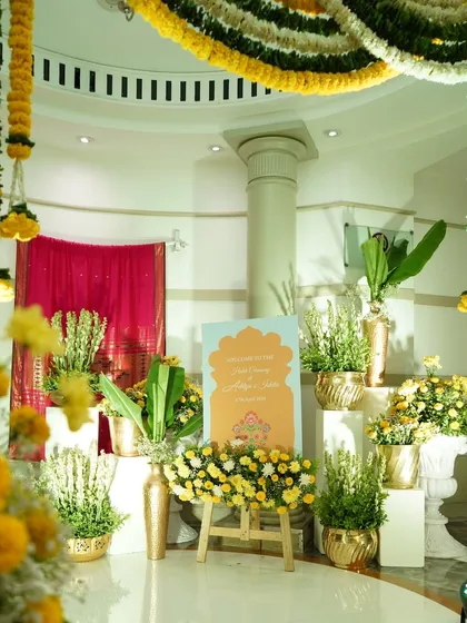 A bright and cheerful welcome area for a Haldi or Mehendi ceremony, with a custom sign, marigold garlands, and traditional brass pots.