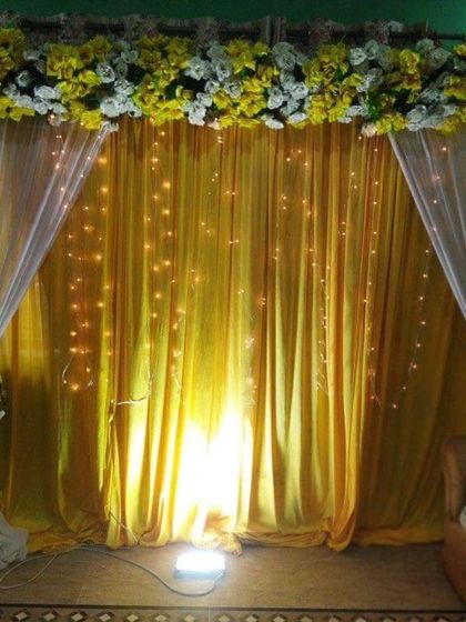 A simple backdrop for a home function, using yellow and white drapes with a floral top border. The warm lighting from below creates a cozy and inviting atmosphere.