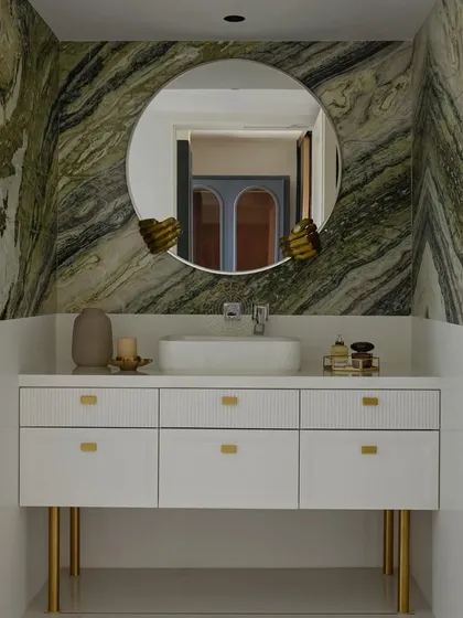 The highlight of this bathroom is the stunning green-veined marble backsplash. The white vanity with gold hardware and legs provides a clean, bright contrast, while the sculptural mirror holders add a unique, artistic touch.