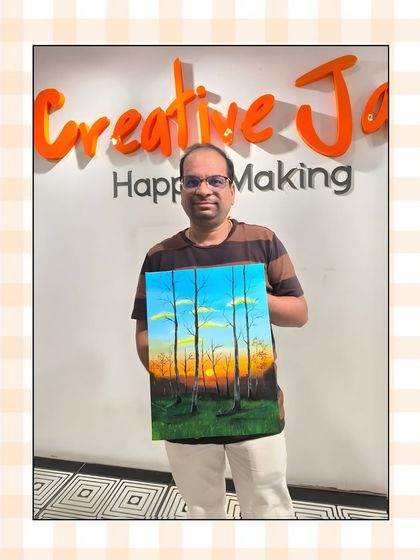 A participant holds up his beautiful landscape painting of a forest at sunset, capturing the warm glow of the sky through the trees.