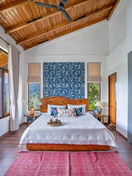 A master bedroom in the villa, featuring a high, wood-paneled ceiling, a custom wooden bed, and a bold blue floral wallpaper that adds a touch of drama.