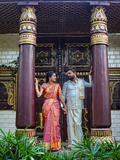 A grand portrait of a couple in traditional attire, framed by the large, dark wood pillars of our Chettinad-style set.