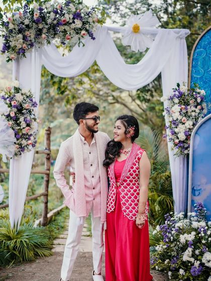 A happy portrait of the couple at their outdoor Haldi event, framed by floral decorations.