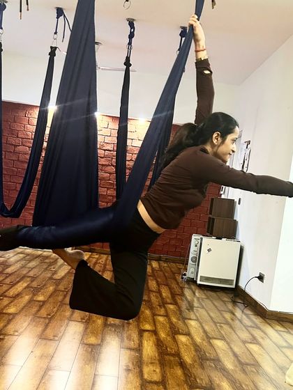 A student gracefully holds an aerial warrior pose. This variation challenges balance and strengthens the legs and core.