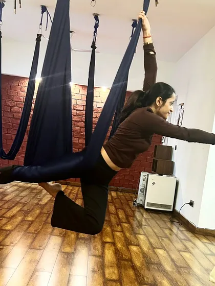 A student gracefully holds an aerial warrior pose. This variation challenges balance and strengthens the legs and core.