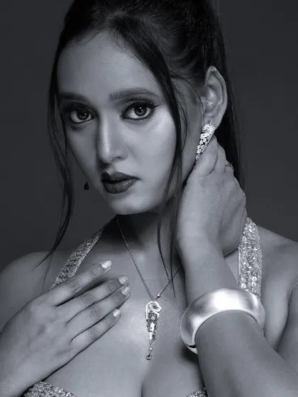 A close-up black and white portrait focusing on jewellery and a dramatic expression. The monochrome tones highlight the sparkle of the necklace and earrings.