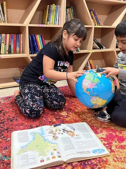 Learning together is always more fun. Here, two children are exploring the world with a globe and an atlas, sharing interesting facts they discover along the way.