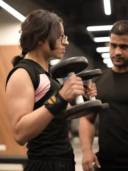 A trainer provides close supervision and guidance to a member performing hammer curls, ensuring her form is perfect for maximum bicep engagement and injury prevention.