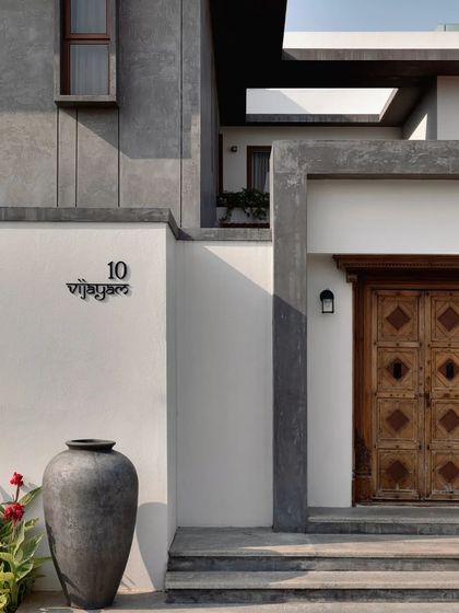A traditional carved wooden door and a large urn mark the entrance, blending cultural elements with modern architectural forms.