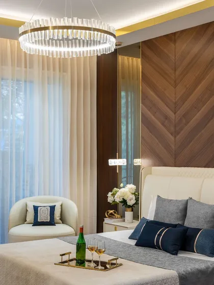 This master bedroom is a testament to refined relaxation. We designed a feature wall with chevron-patterned wood paneling to add warmth and texture. The space is crowned by a stunning crystal ring chandelier, creating an ambiance of pure elegance and comfort.