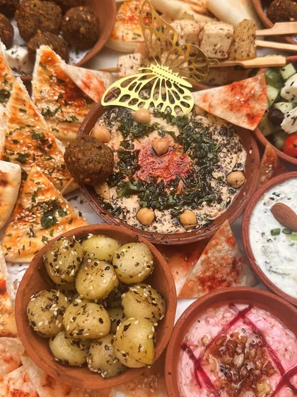 A close-up of a bountiful Mezze platter, showcasing the textures of loaded hummus, beetroot dip, falafel, and za'atar-spiced potatoes.