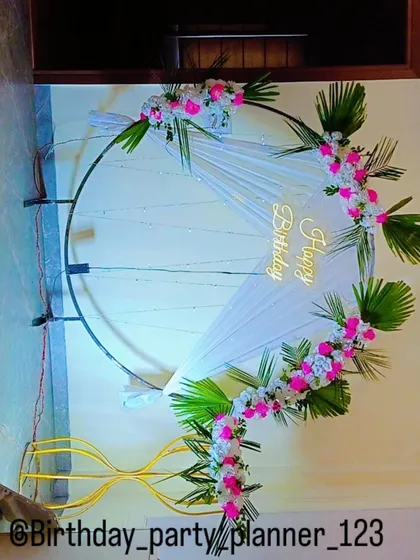 An elegant birthday ring decoration using fresh flowers, palm leaves, and a golden 'Happy Birthday' sign.