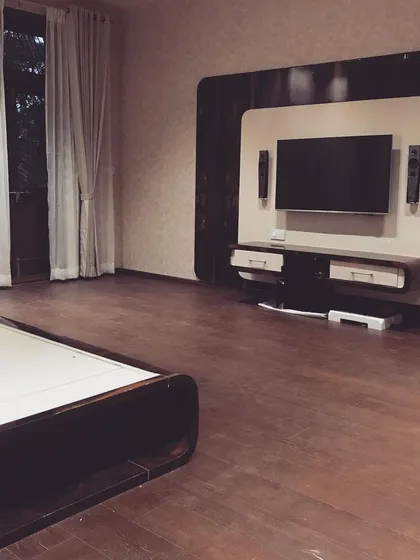 A minimalist entertainment wall in a spacious bedroom, featuring a floating console and a curved back panel. The design keeps the focus on the screen while providing essential storage.