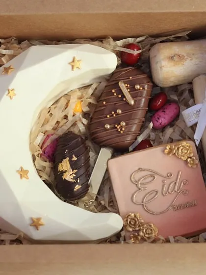 Another view of the Eid piñata box, showcasing the crescent moon, a cakesicle, a decorated cookie, and a stuffed date. This shows the variety of treats included in this special gift.