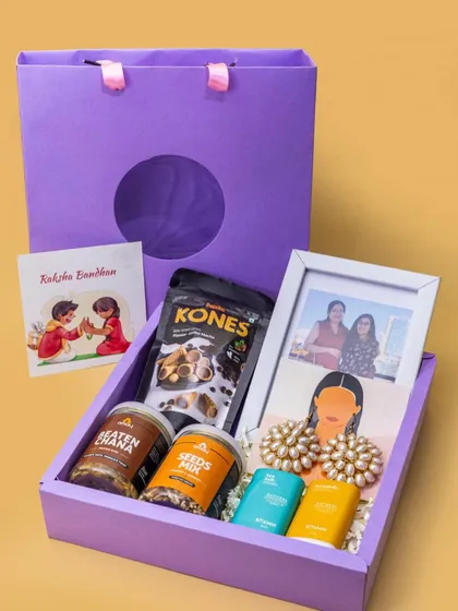 I believe gifts should be personal. This Rakshabandhan hamper for a sister includes healthy snacks like seeds and beaten chana, fun earrings, and a personalized photo frame to capture a favorite memory. It comes packed in a beautiful purple gift bag, ready to make her day.