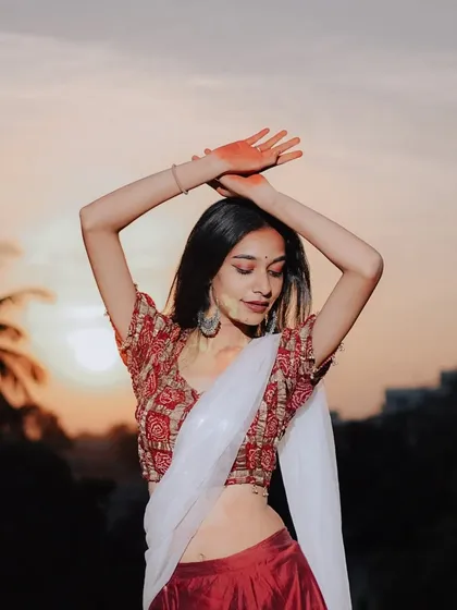 A portrait capturing the joy of Holi, with the model's arms raised against the sunset, her hands and face lightly dusted with color.
