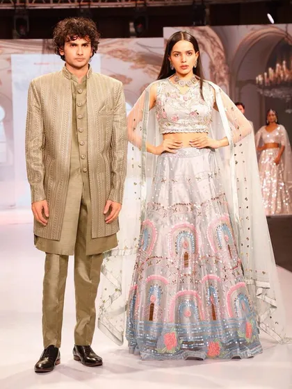 A high-fashion runway look available for rent. This features a modern, structured olive green Indo-Western for him and a pastel blue lehenga for her.