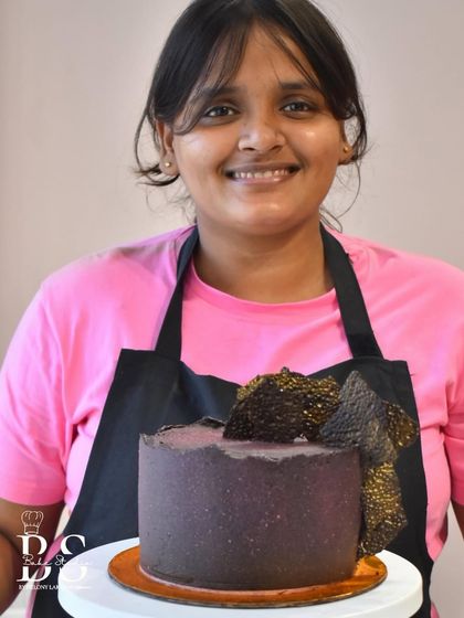 A student proudly holding her chocolate ganache cake, demonstrating the skills she learned in class.