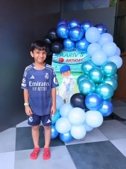 The birthday boy stands proudly by his cricket-themed welcome sign. It's his special day to shine.
