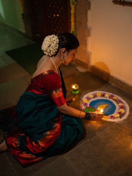 A woman lighting a diya by her rangoli. This photo captures a quiet, traditional moment of Diwali, using the gentle candlelight to create a soft and intimate mood. The gajra in her hair adds a classic touch.