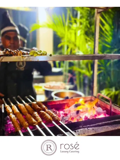A chef tends to kebabs on a live charcoal grill at an outdoor event. This image captures the smoky, authentic flavor we bring to our grilled Indian delicacies.