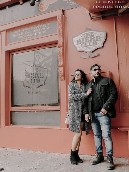 A wide shot of a couple in fashionable winter coats posing in front of 'The Biere Club', capturing the urban-chic aesthetic.