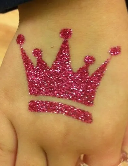 A bold pink glitter crown tattoo on the hand. This is the perfect design for the birthday girl or anyone who wants to feel like royalty for the day.