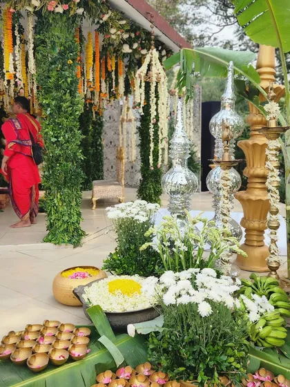 Embracing tradition with hues of gold and green. This corner of a South Indian wedding features tall diyas, silver lamps, and bowls of flowers set on banana leaves, creating a culturally rich and graceful display.