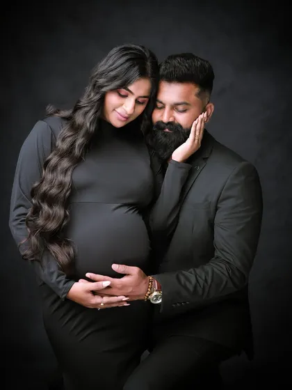 We capture the deep connection between partners with classic, intimate portraits like this one. This couple's portrait, set against a simple dark backdrop, emphasizes emotion and the shared excitement of expecting.