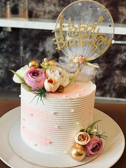 A delicate and dreamy birthday cake. The design features a soft pink ombre, fresh flowers, and a glittery topper with a tulle bow, adding a touch of sparkle to the special day.